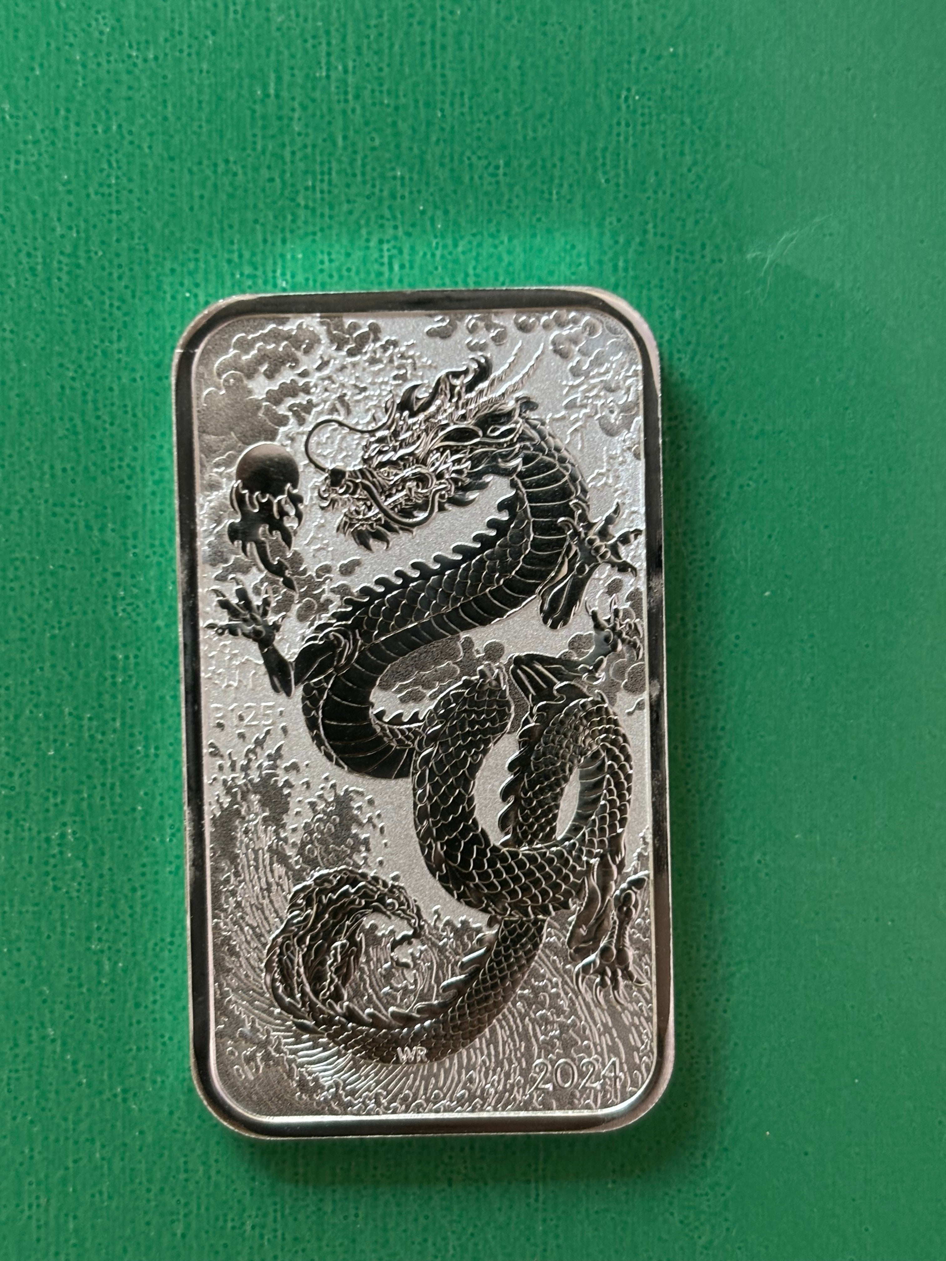 A 1oz .9999 silver bar from Perth Mint features a raised dragon design with clouds and flames on a green textured background. The year 2024 appears in the lower right corner.