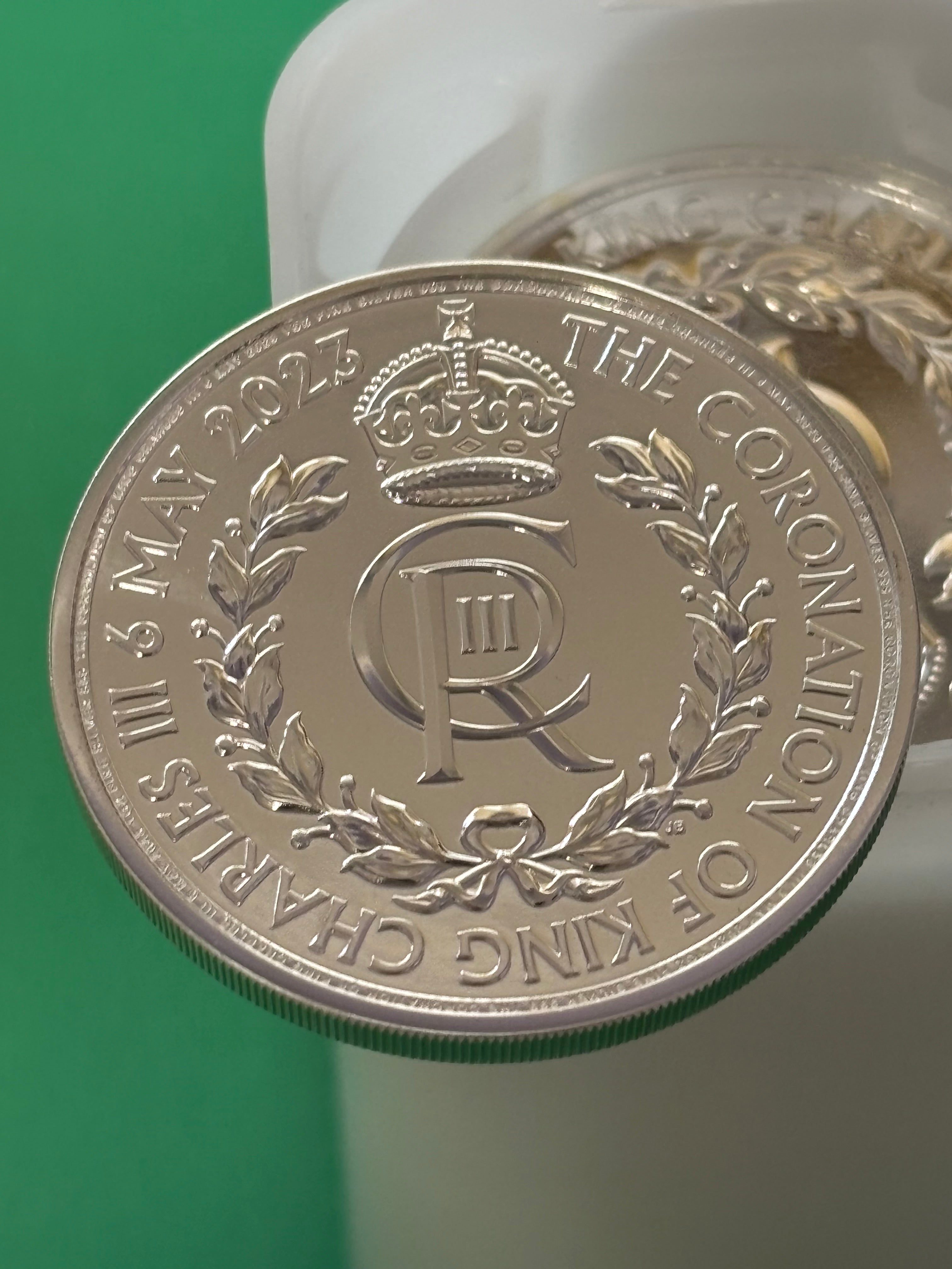 A close-up of the 1oz .999 Silver Coin Charles III Coronation, showing a crowned CR monogram, laurel wreath, and "THE CORONATION OF KING CHARLES III 6 MAY 2023" inscription on a green background.