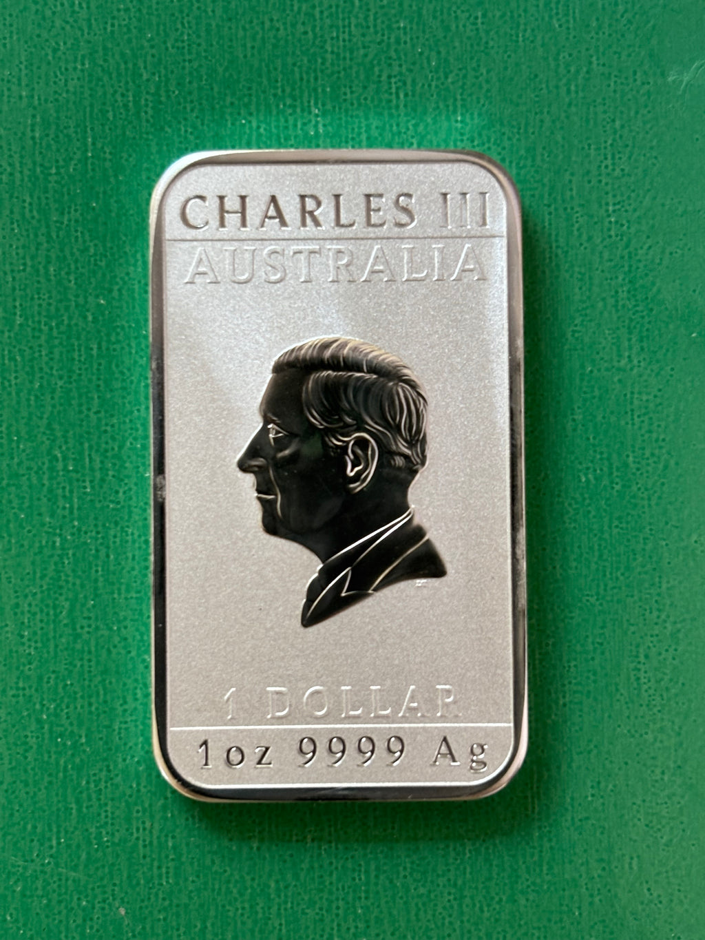 A rectangular 1oz .9999 Silver Bar Perth Mint Dragon 2024, featuring a profile of a man with the text CHARLES III AUSTRALIA, 1 DOLLAR, and 1 oz 9999 Ag on a green background.