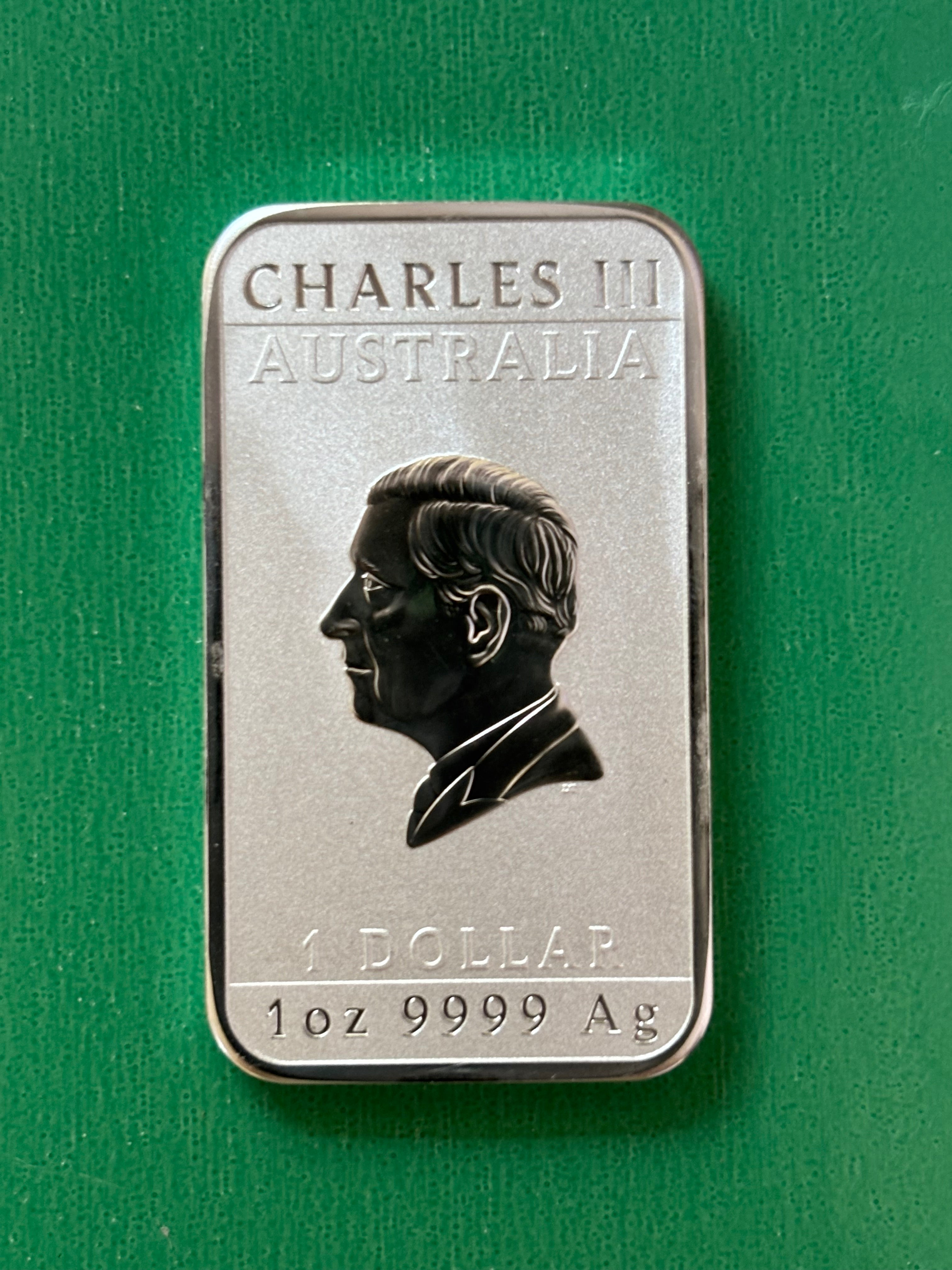 A rectangular 1oz .9999 Silver Bar Perth Mint Dragon 2024, featuring a profile of a man with the text CHARLES III AUSTRALIA, 1 DOLLAR, and 1 oz 9999 Ag on a green background.