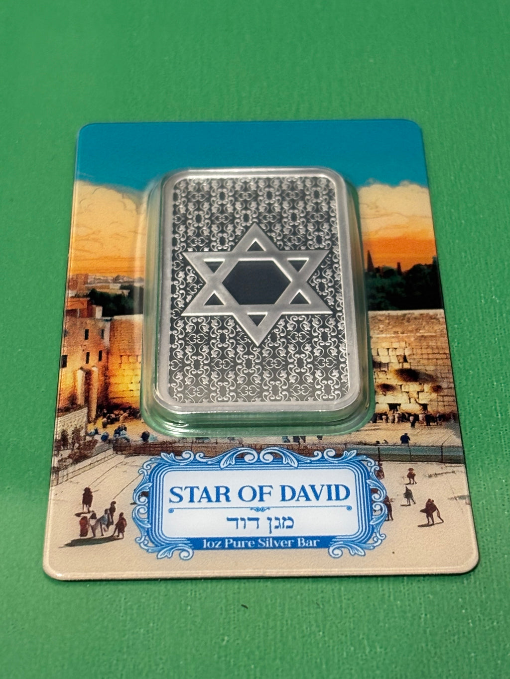The 1oz .999 Silver Bar PAMP Star Of David features the Star of David and rests on packaging depicting Jerusalem's Western Wall, with a label displaying "Star of David" in both English and Hebrew.