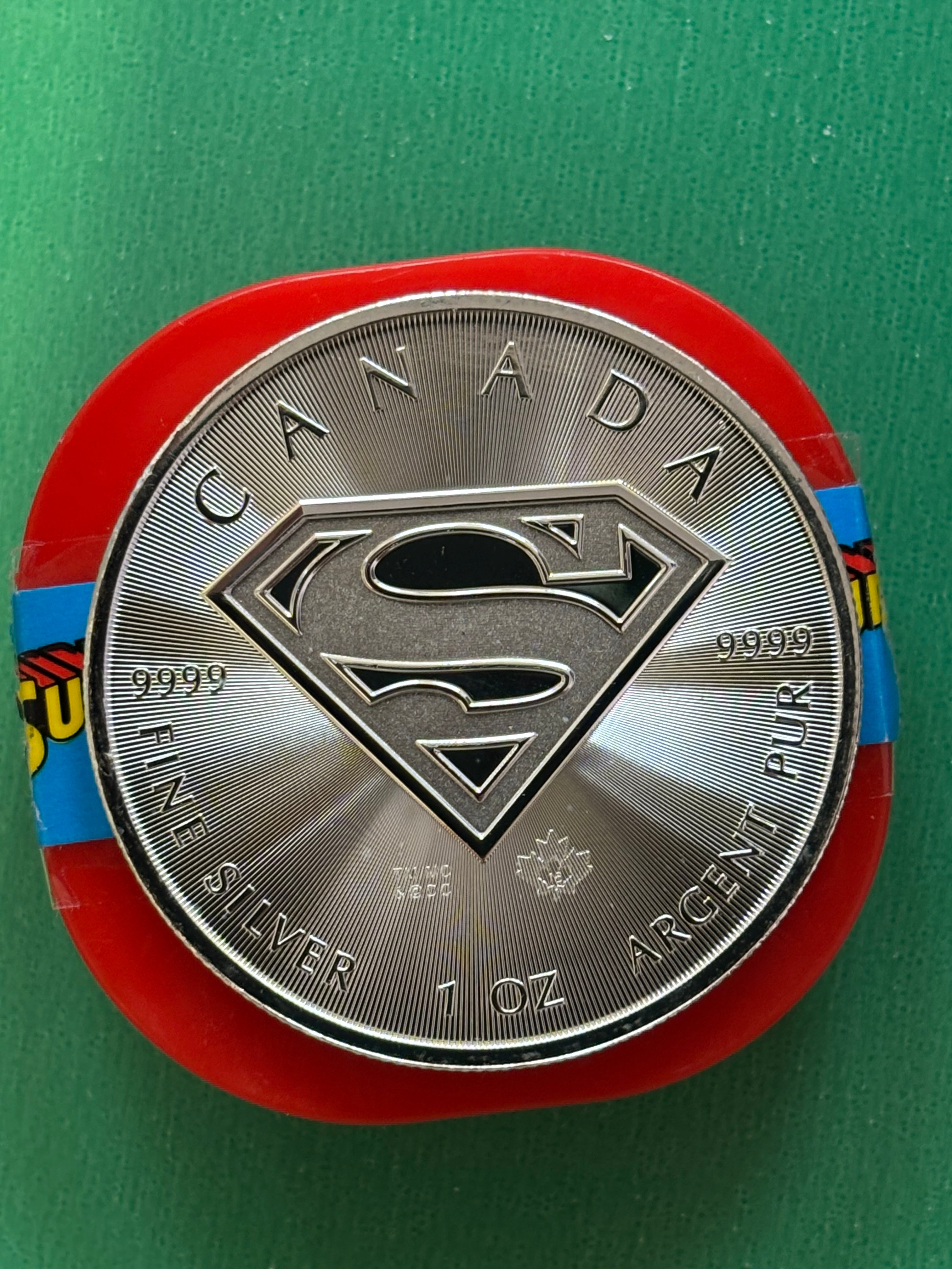 The 1oz .9999 Silver Coin Superman features the iconic Superman logo at its center, encircled by CANADA, FINE SILVER 1 OZ ARGENT PUR, 9999, and a small maple leaf, shown on a green background.