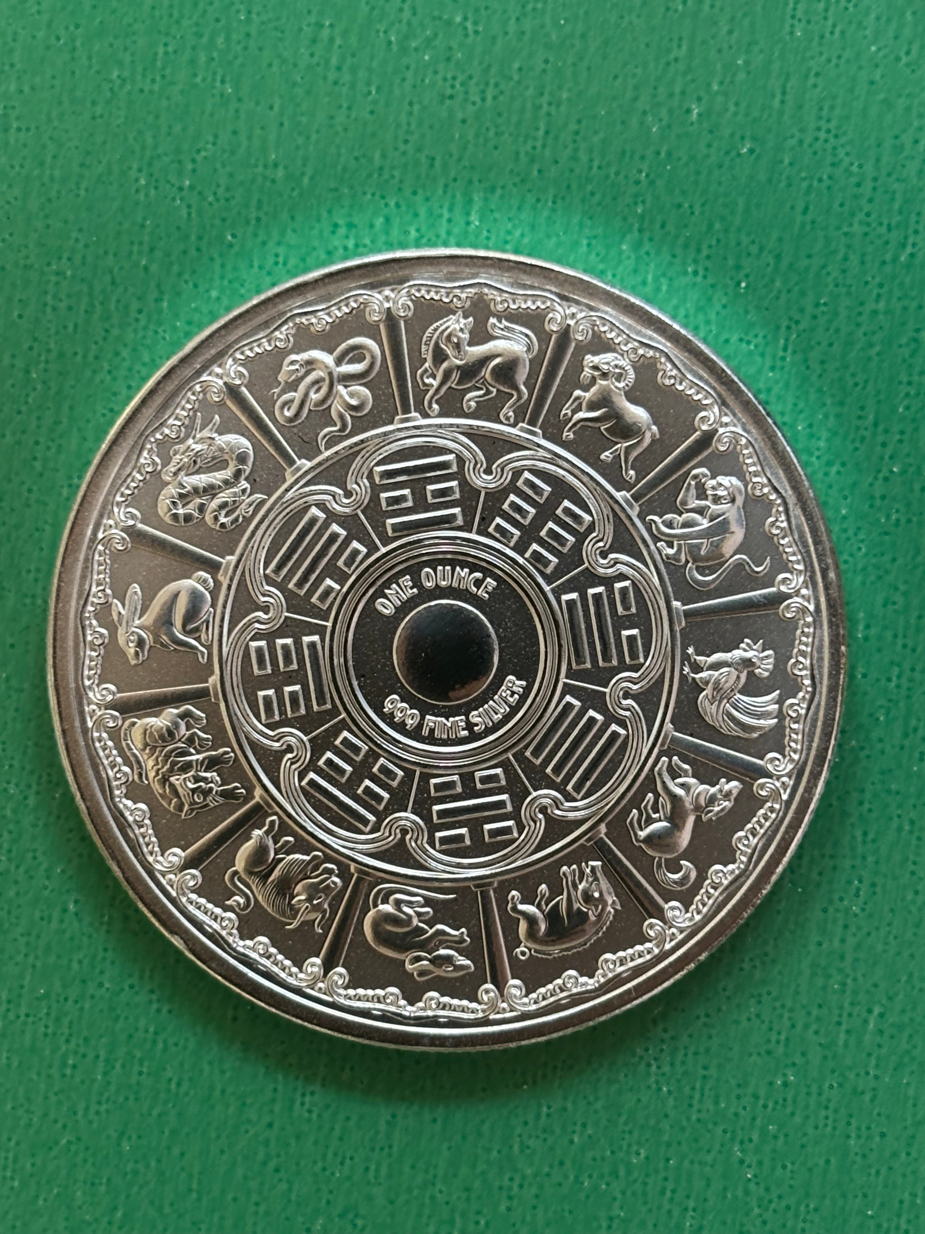 The 1oz .999 Silver Year Of The Snake 2025 coin features the twelve Chinese zodiac animals around the edge, detailed patterns, and “ONE OUNCE 999 FINE SILVER” at the center on a green background.