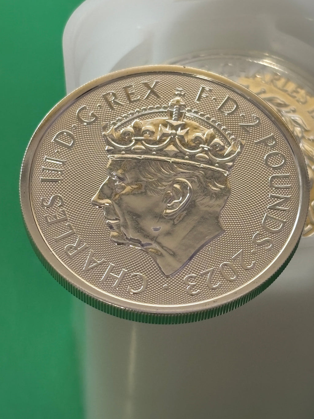 A close-up of the 1oz .999 Silver Coin Charles III Coronation, displaying King Charles III’s crowned profile and the inscription CHARLES III D G REX F D 2 POUNDS 2023, set against a green and white background.