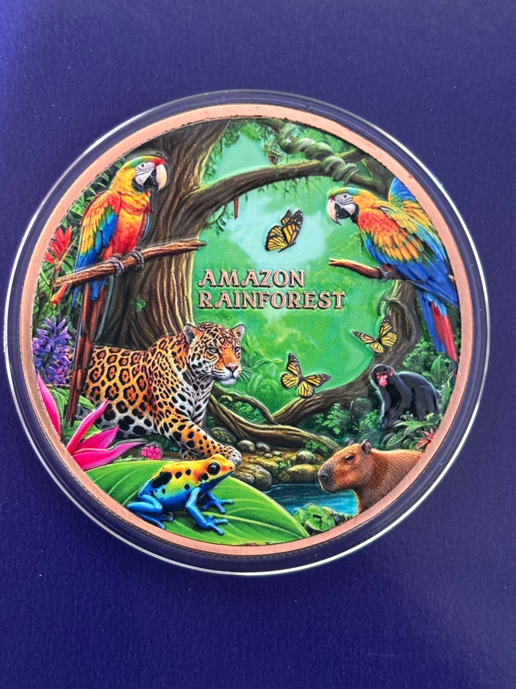 A vibrant 1oz ADVP Copper Round titled "Amazon Rainforest" features a jaguar, parrots, capybara, poison dart frog, butterflies, and lush green jungle plants in a circular design.