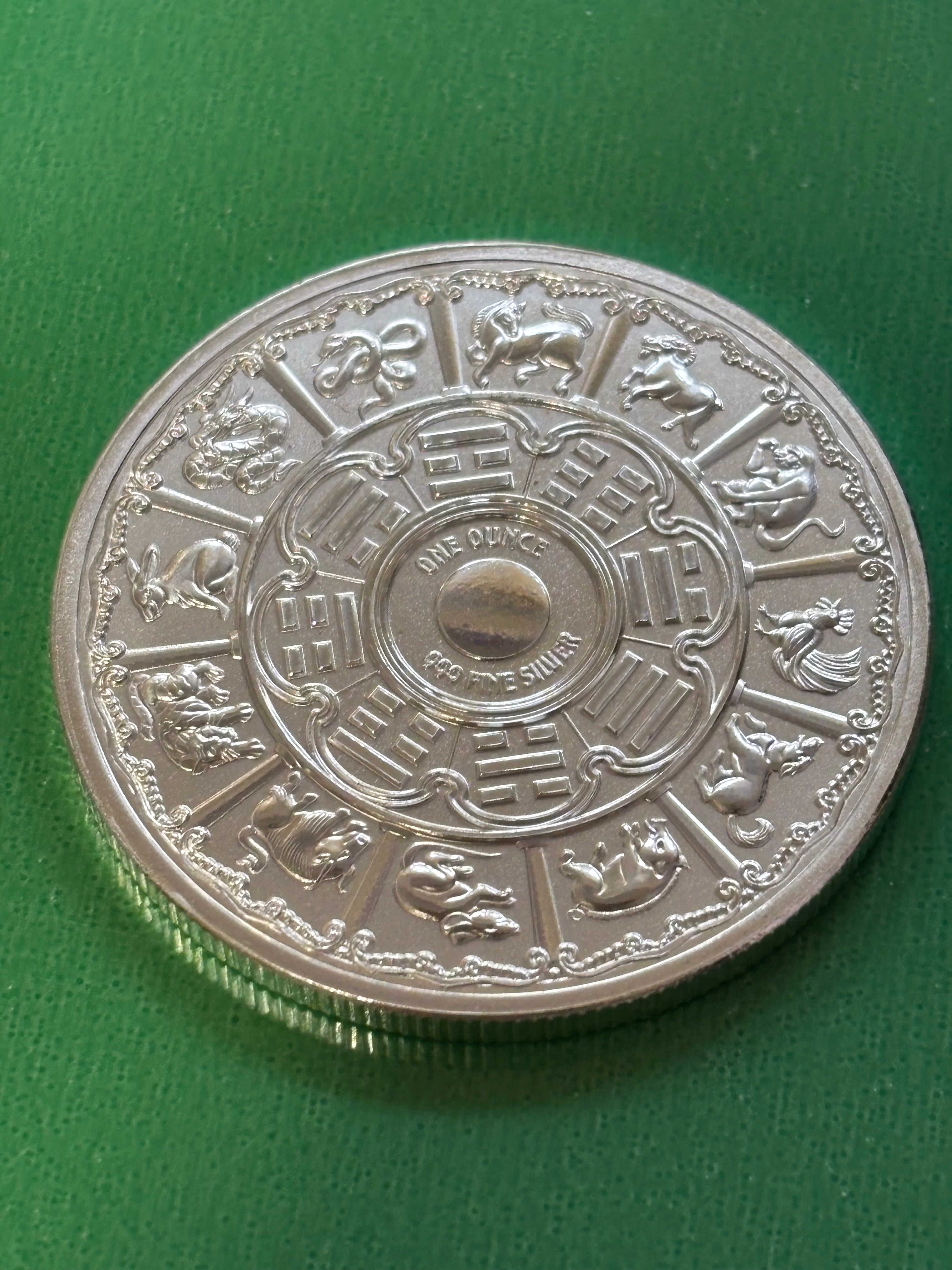The 1oz .999 Silver Year Of The Snake 2025 coin shows Chinese zodiac animals in a circle and ornate central patterns, displayed on a green textured background.