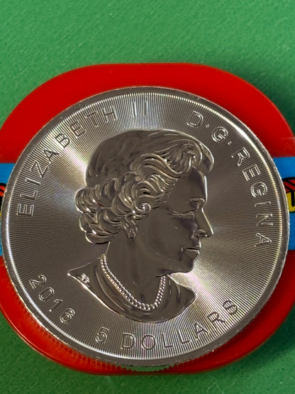 A close-up of a 1oz .9999 Silver Coin Superman, featuring the hero’s emblem and set against a red and green background. The coin is inscribed with ELIZABETH II D·G·REGINA and dated 2016.